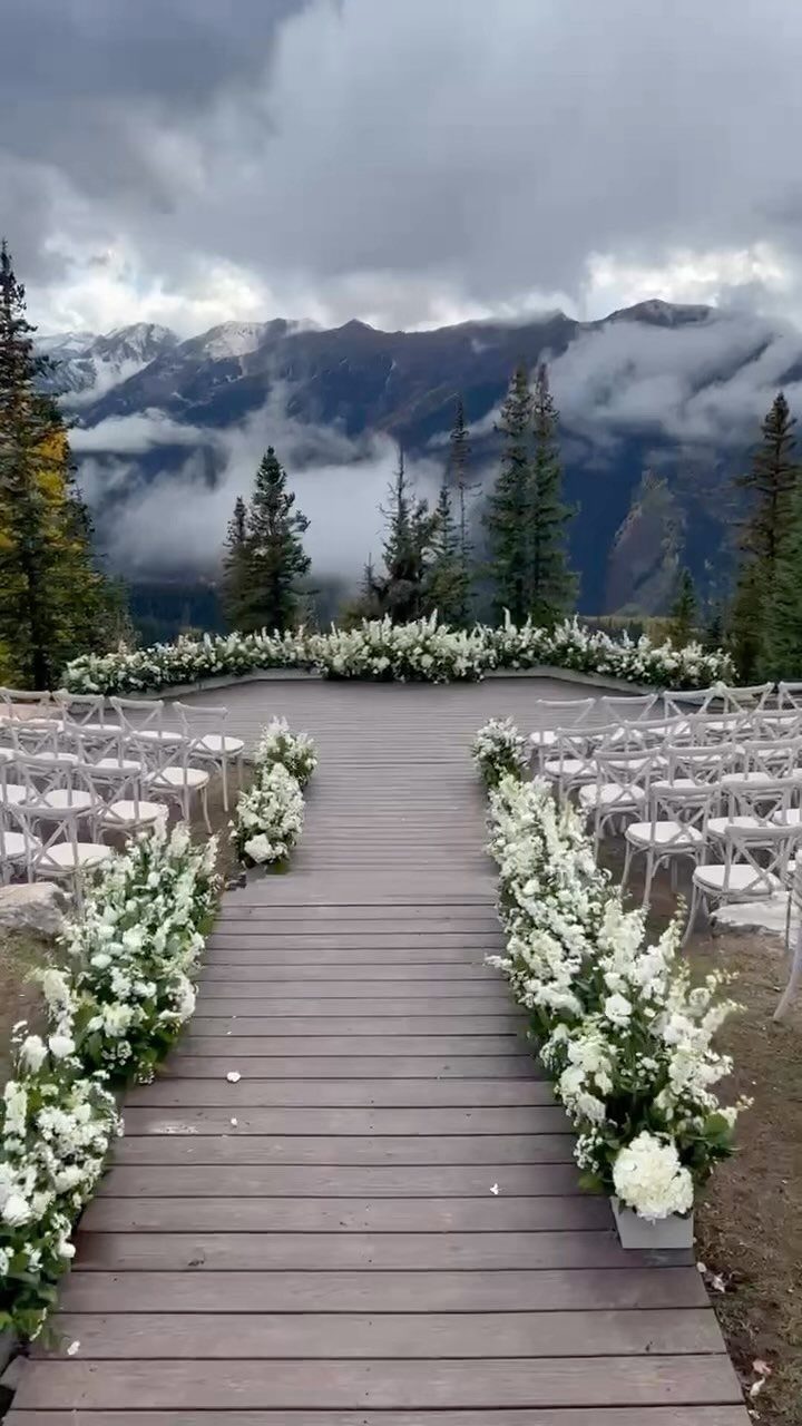 Wooden wedding aisle with white flowers overlooking a cloudy mountain landscape