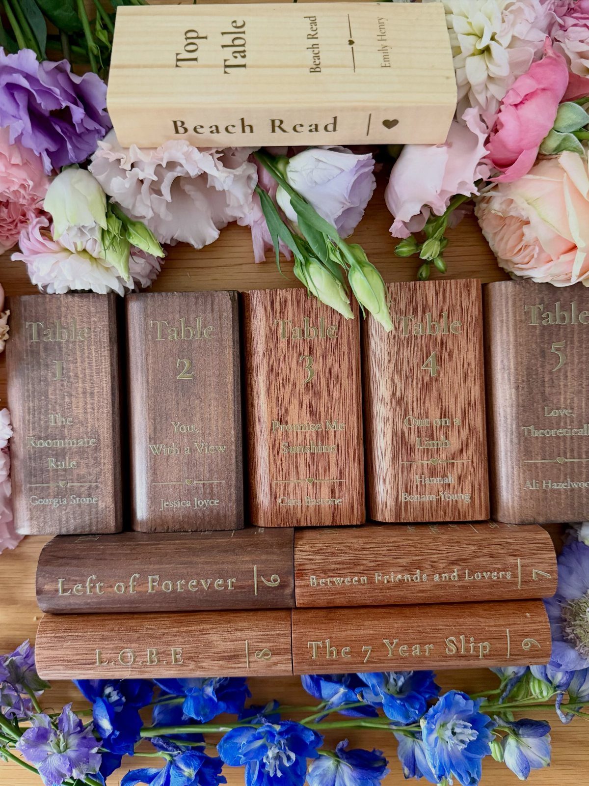 Wooden book-shaped table numbers surrounded by colorful spring flowers on a wooden surface.