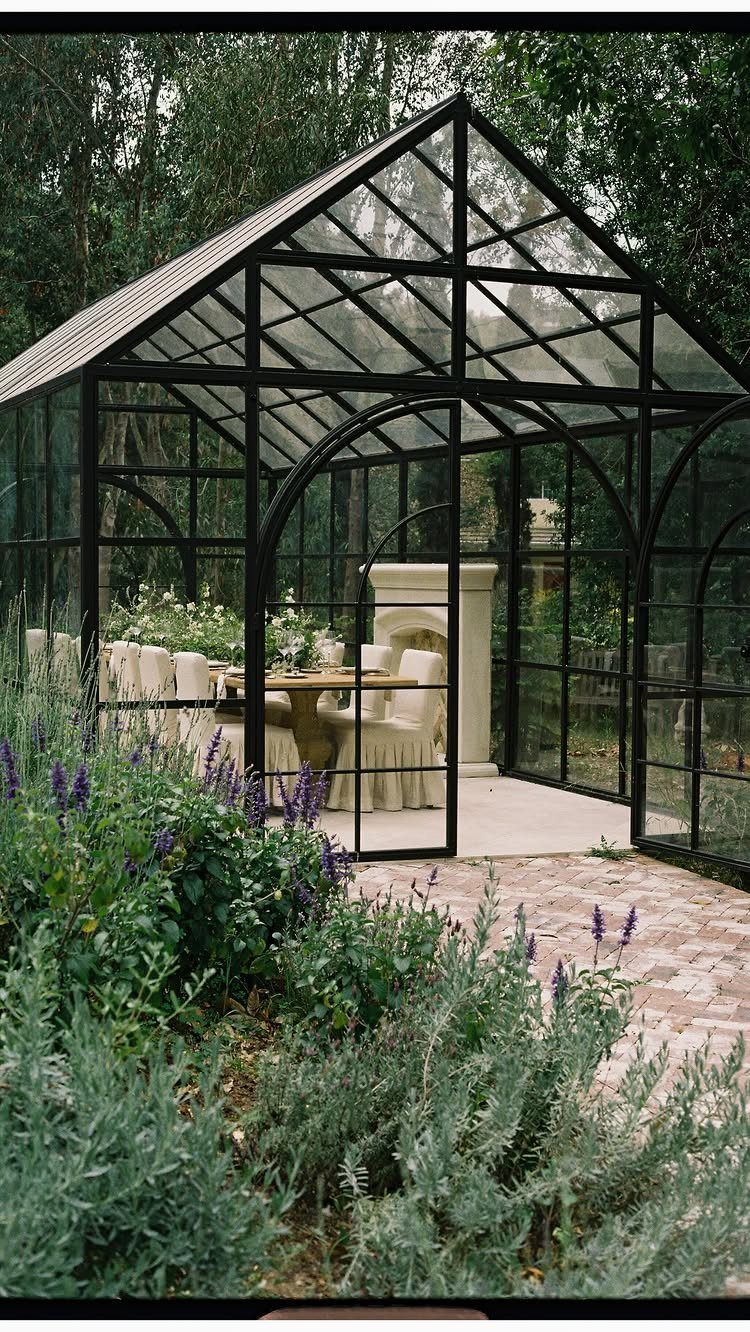 Glass greenhouse with a dining table and chairs surrounded by garden greenery
