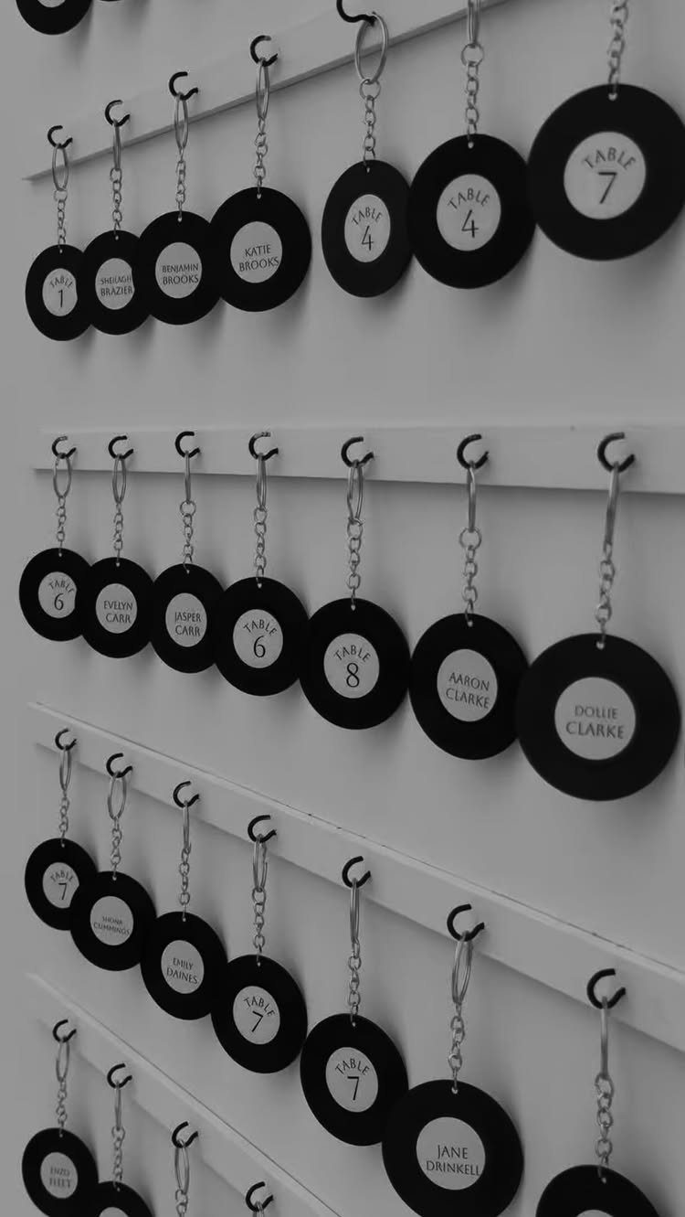 Black circular name and table tags hanging from silver chains on white shelves.
