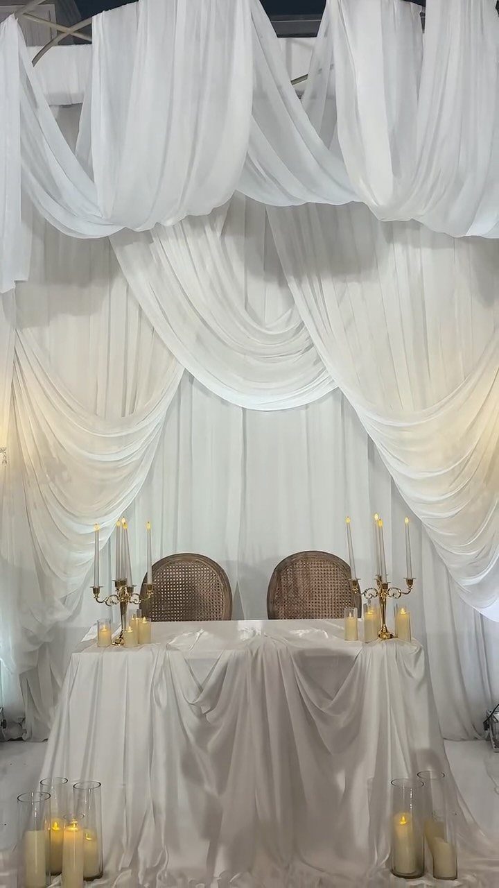 White draped sweetheart table with gold candelabras and white sheer curtain backdrop.