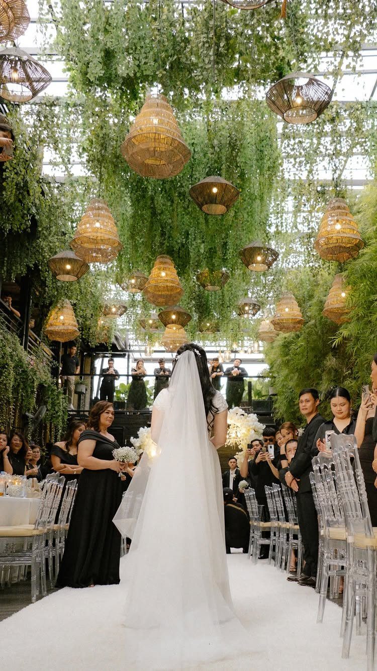Bride in white gown standing at an altar surrounded by guests and hanging greenery