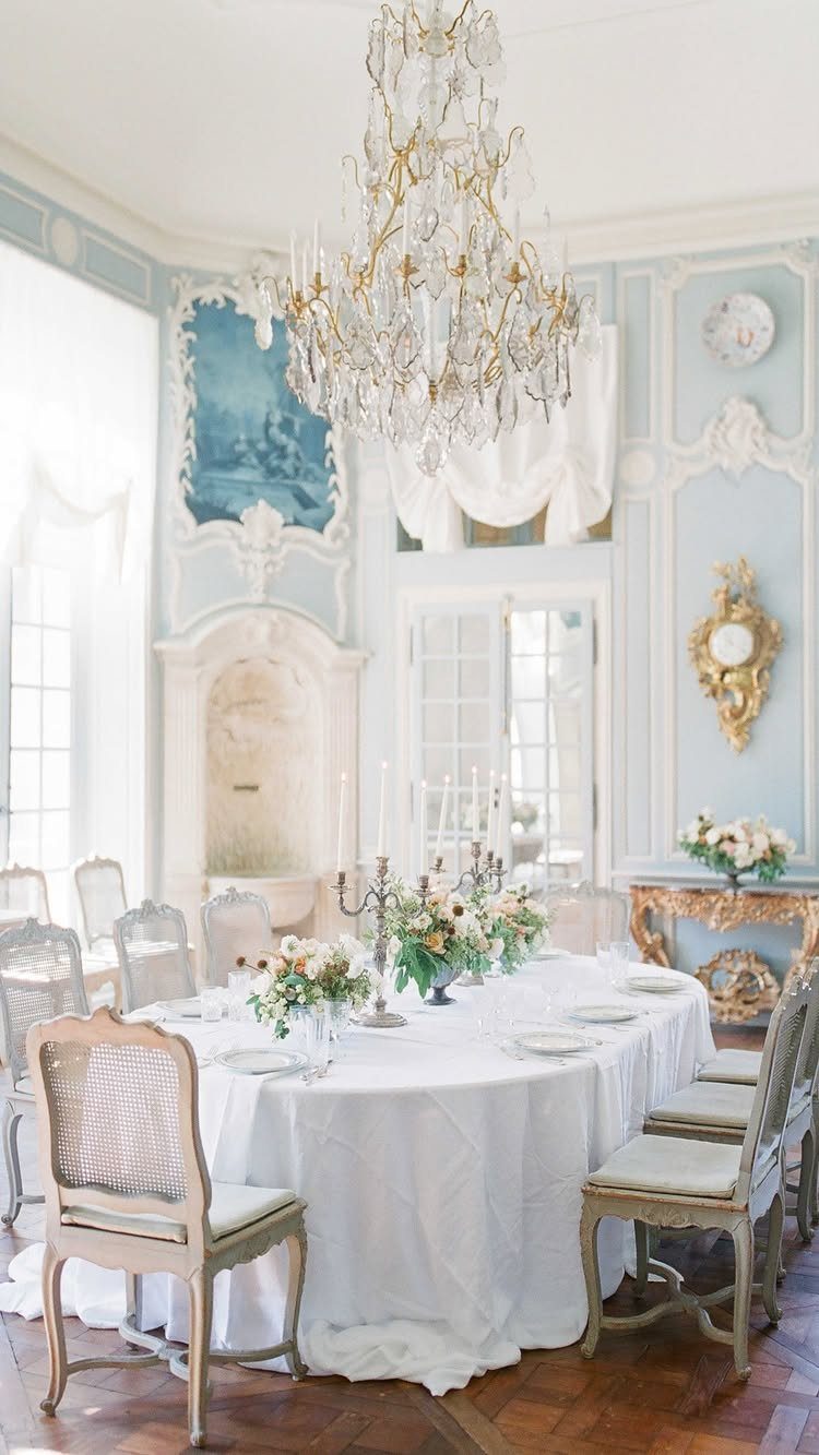 Elegant dining table with white linens and floral arrangements in an ornate room.