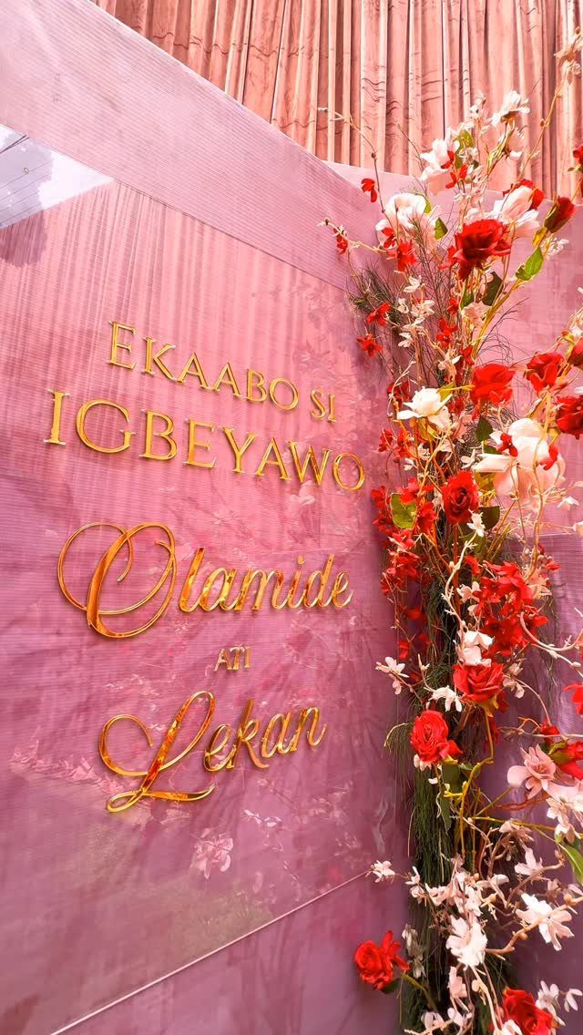 Pink wedding welcome sign with gold lettering and red and white floral accents.