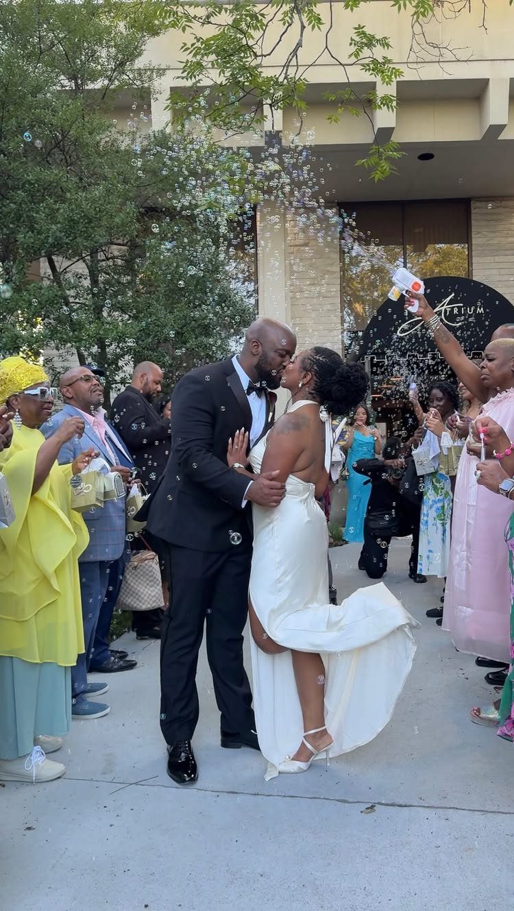 Bride and groom kissing while guests blow bubbles during their wedding exit.