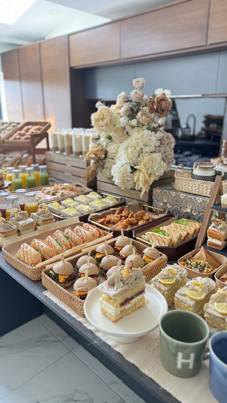 Breakfast buffet spread with mini sliders, sandwiches, and white floral centerpieces on a counter.