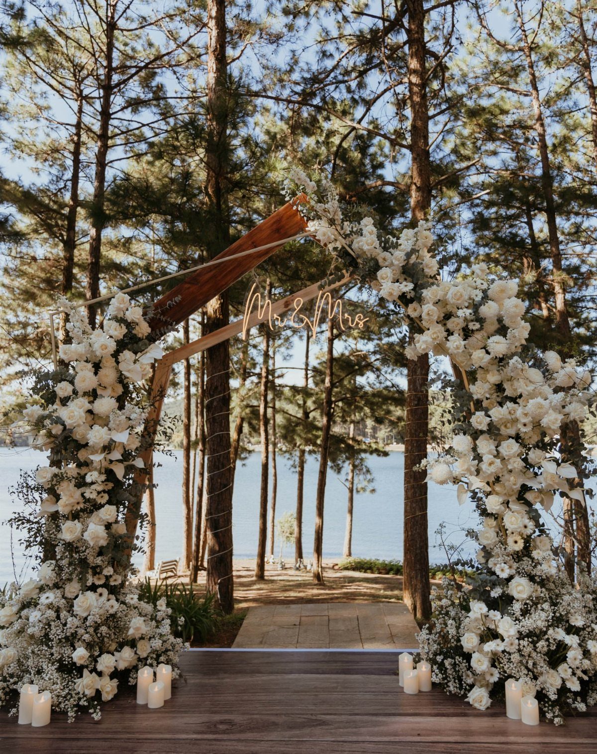Wooden wedding arch with white flowers in a pine forest by a lake