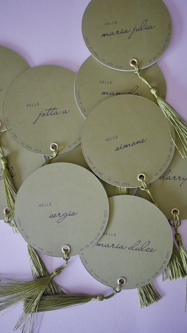 Olive green circular place cards with cursive names and decorative green tassels.