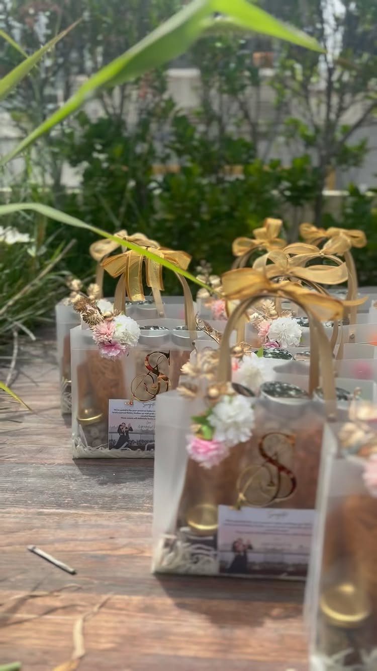 Clear gift bags with gold ribbons and flowers arranged on a wooden deck.