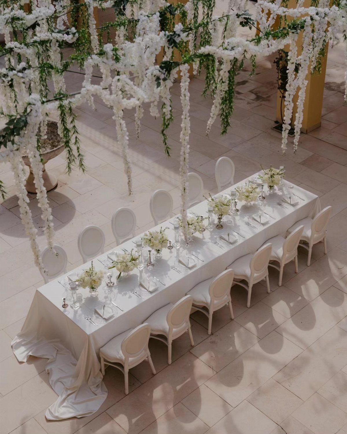 Elegant long wedding table with white linens and floral canopy on stone patio