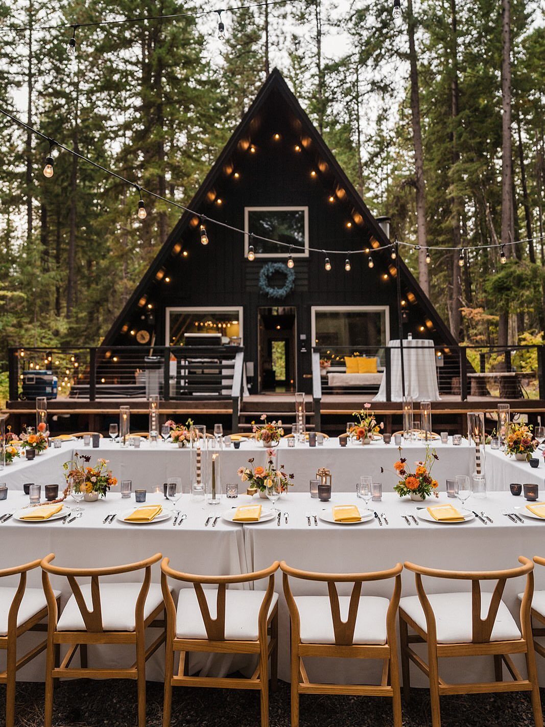 Outdoor wedding reception with white tables and chairs in front of a black A-frame cabin.