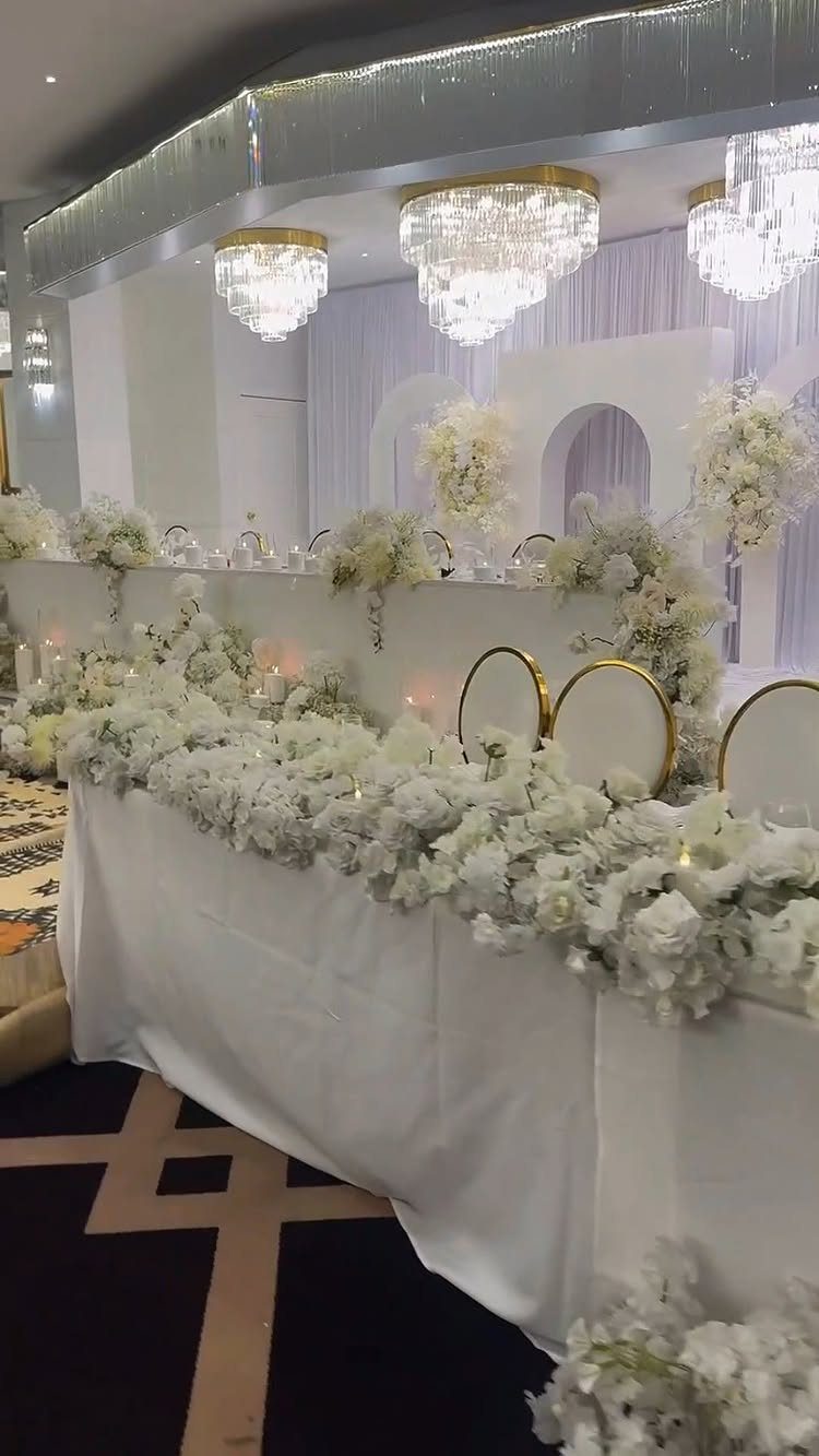 White floral wedding head table in a decorated indoor venue with crystal chandeliers.