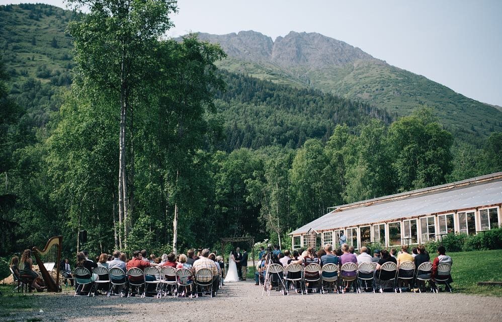 Outdoor wedding ceremony with guests seated before a couple near a mountain lodge.