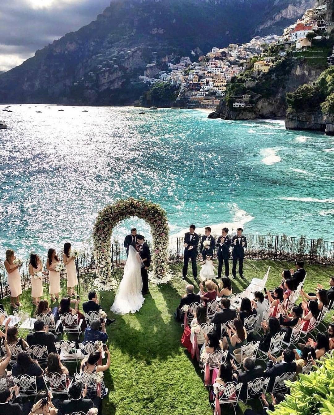 Wedding ceremony on a cliff overlooking the Amalfi Coast with a floral arch.