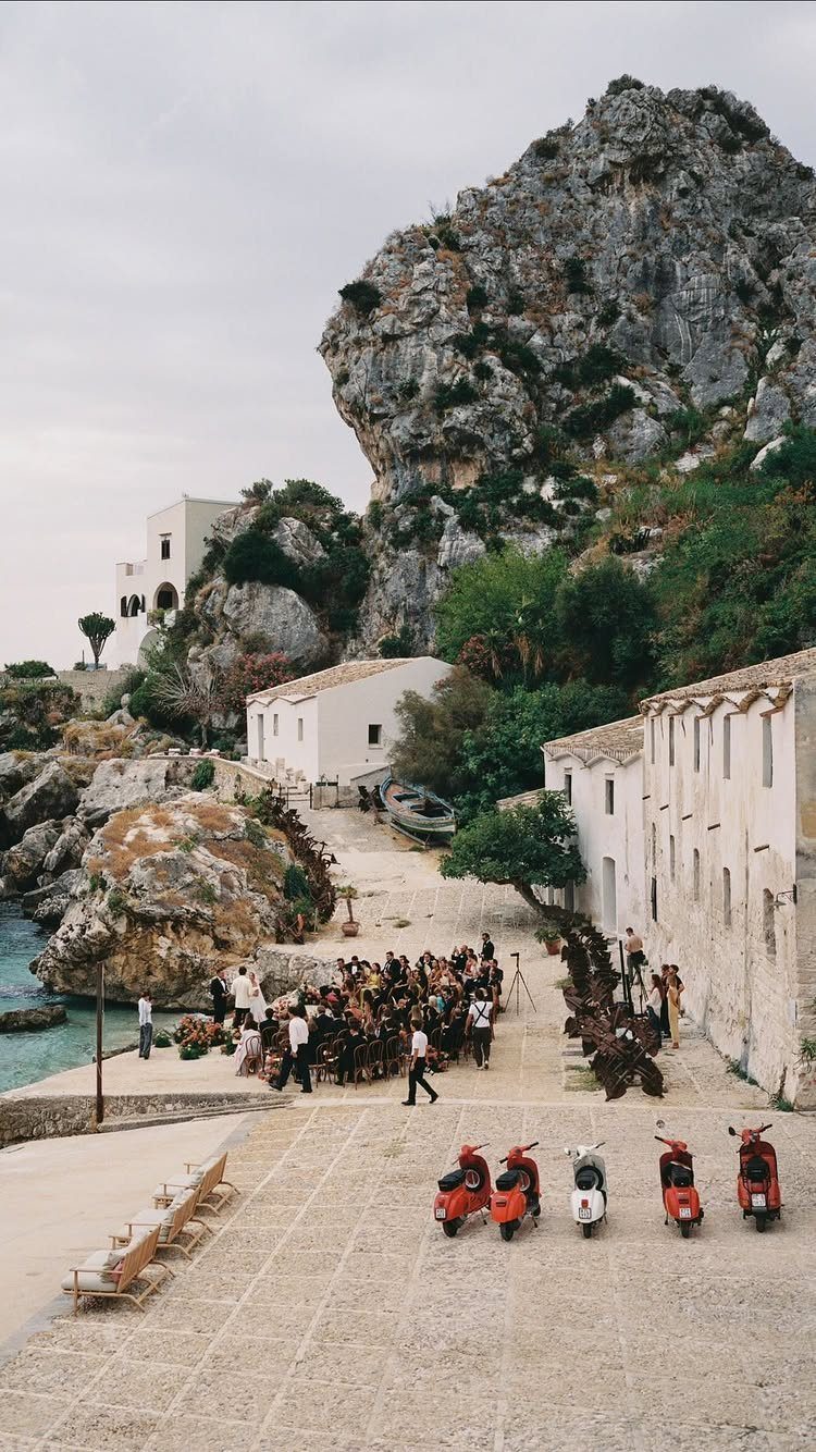 Wedding ceremony in a coastal Italian village with white buildings and red scooters.
