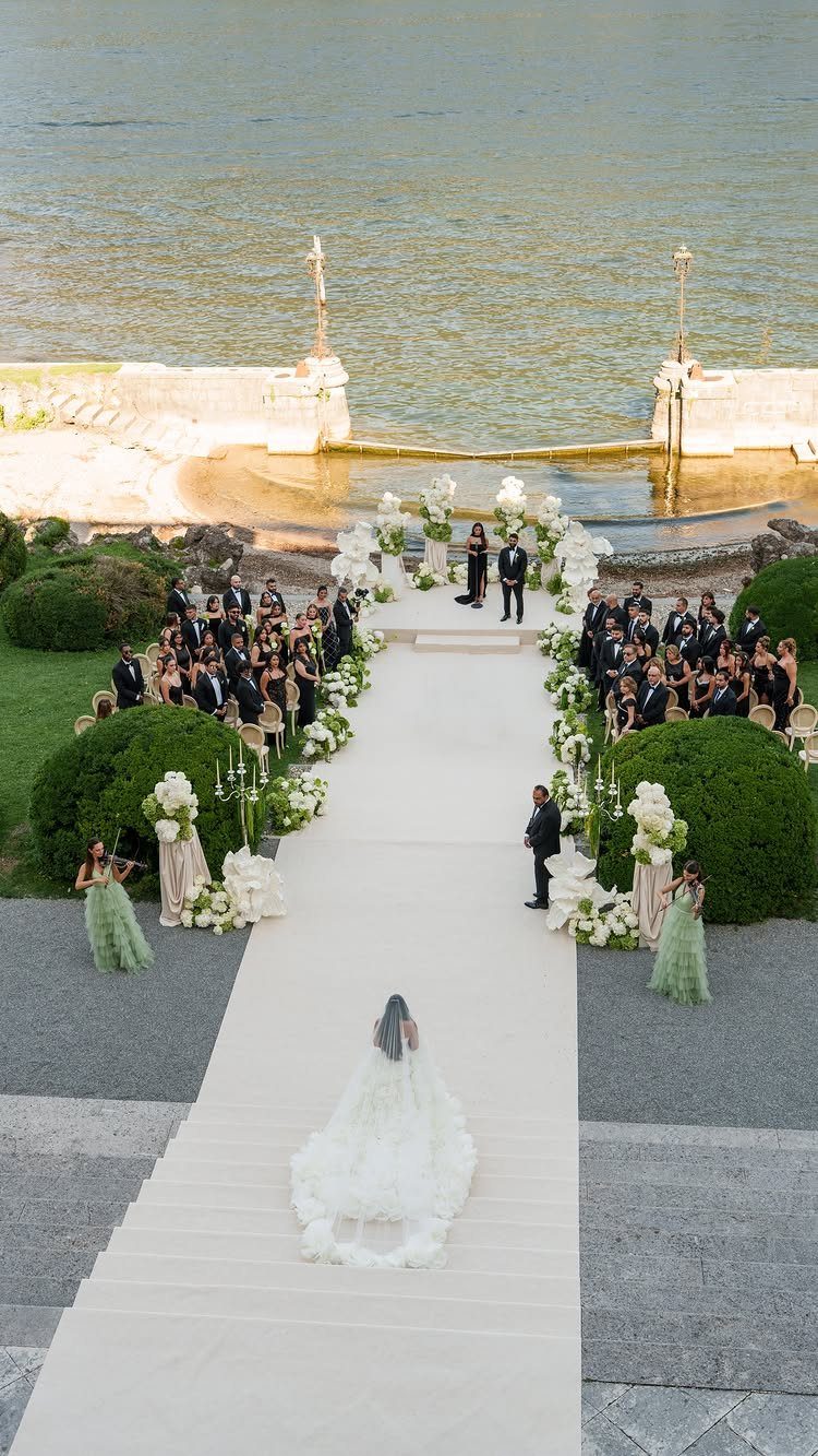 Bride walking down a white aisle at a lakeside wedding ceremony with guests.