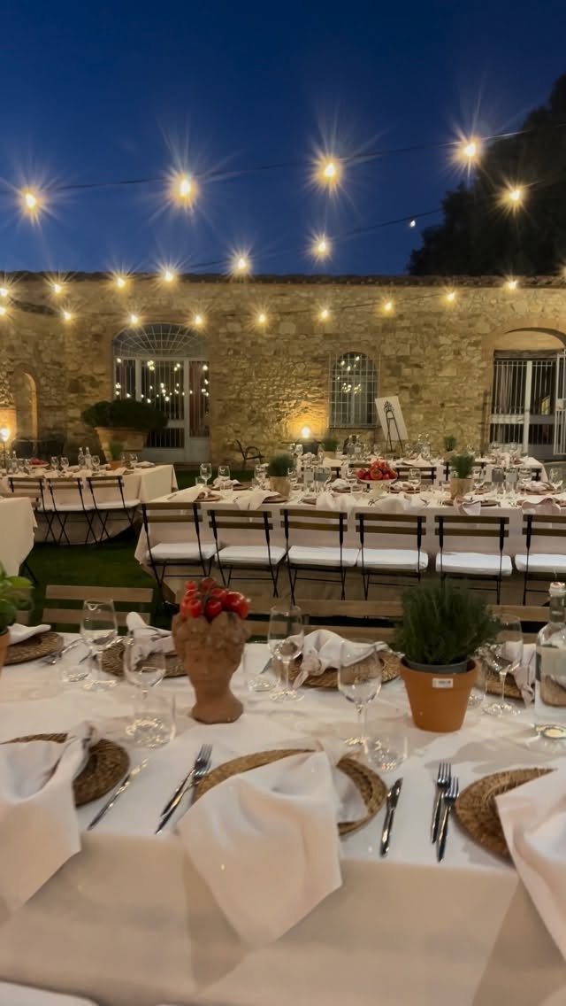 Outdoor wedding reception tables set against a stone villa under evening string lights