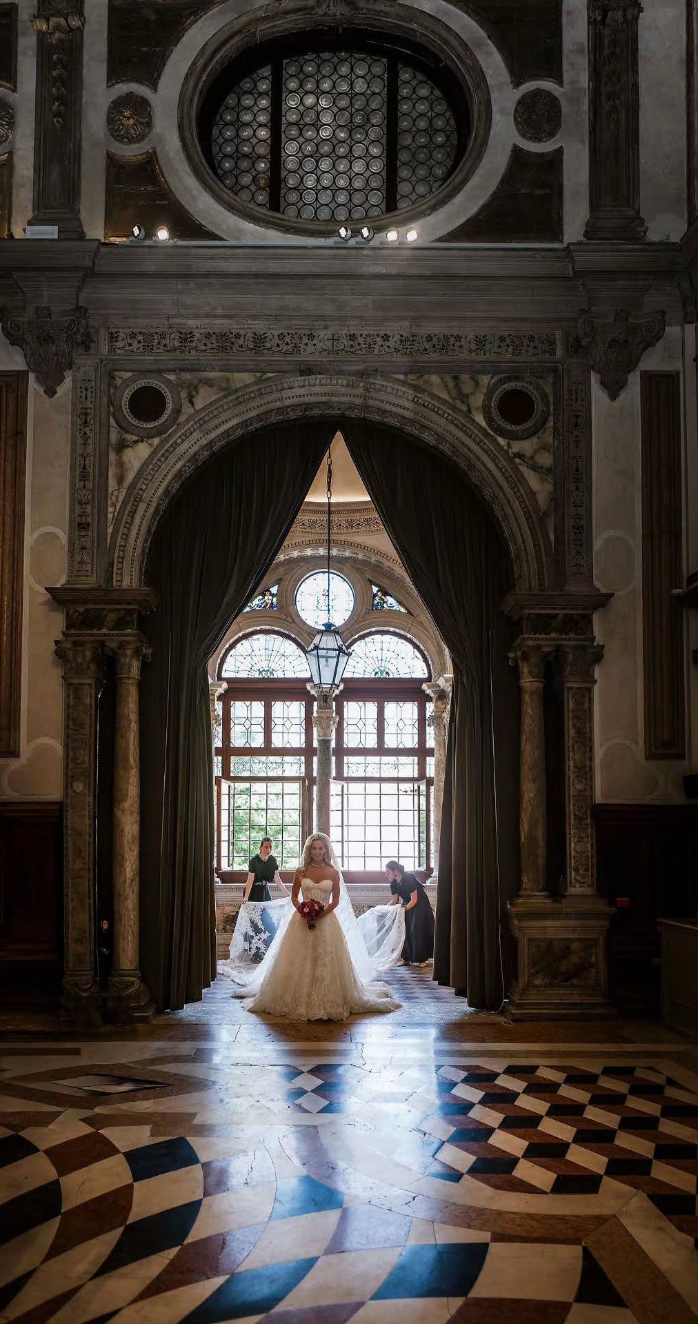 Bride in white gown standing in a grand Venetian palazzo with checkered floors.