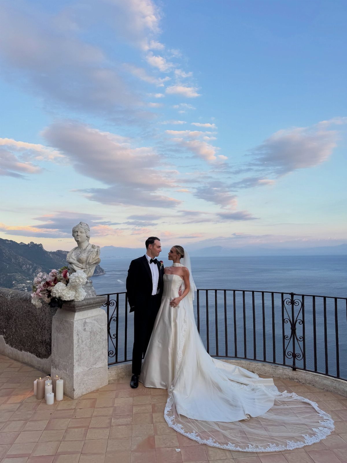 Bride and groom posing on a stone terrace overlooking the Amalfi Coast sea.
