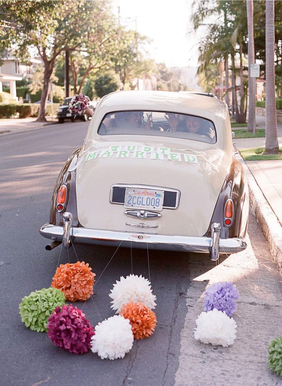 Vintage cream car with colorful pom-poms tied to the bumper trailing behind.