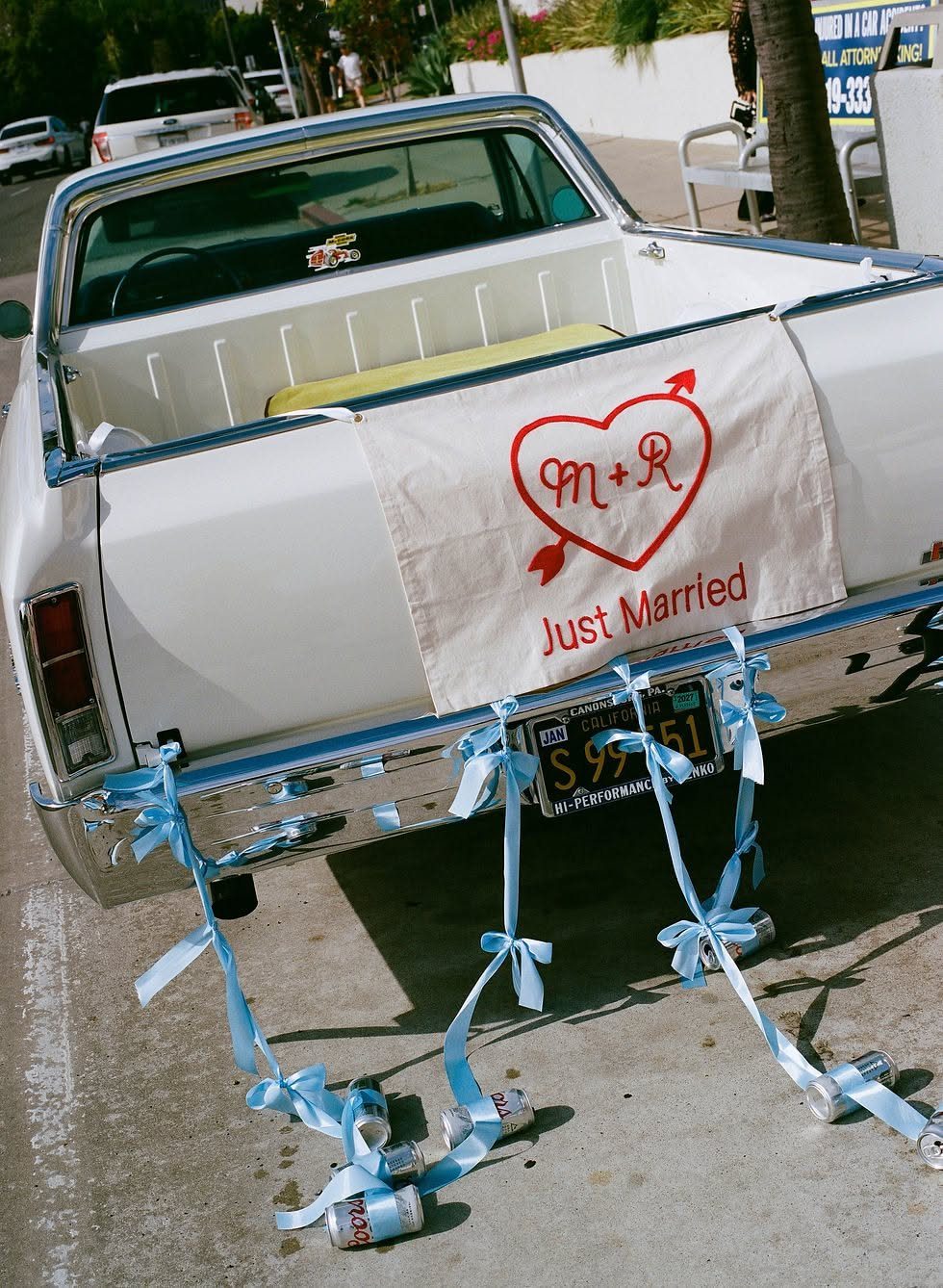 White vintage pickup truck with a Just Married fabric banner and trailing tin cans.