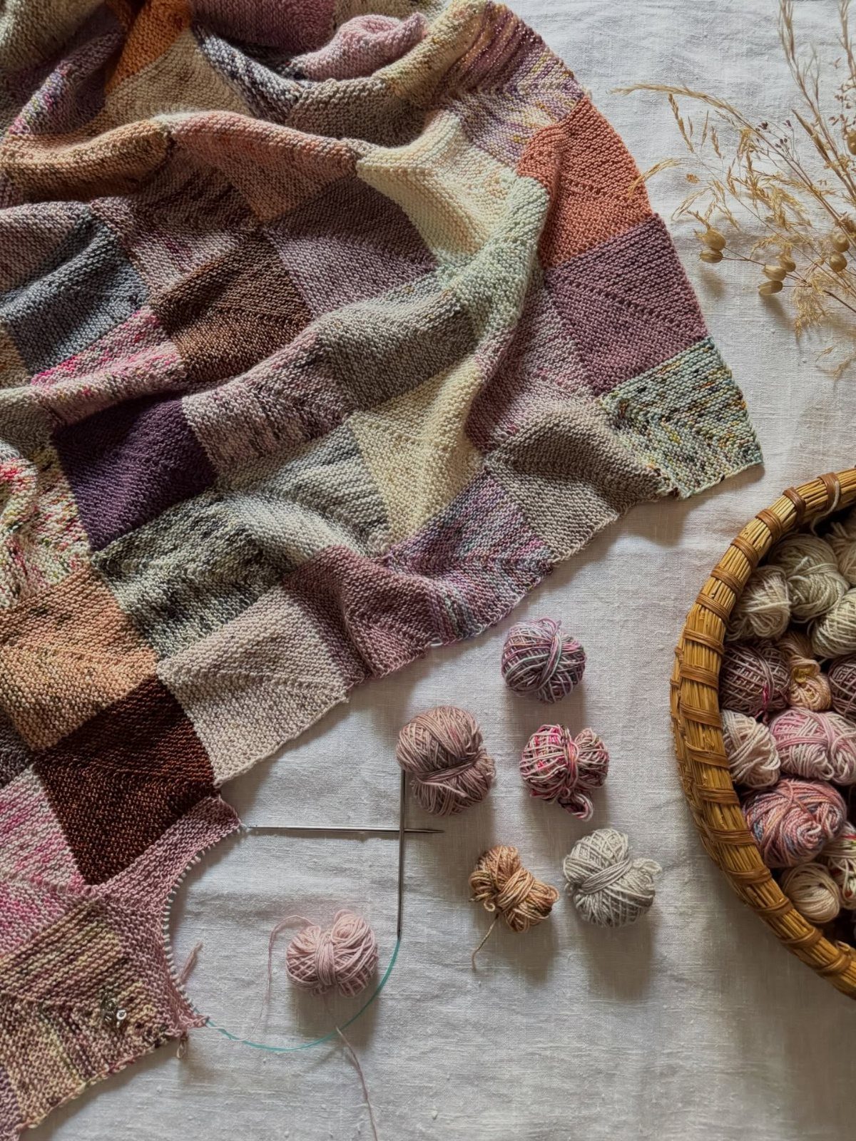 Woven checkered blanket in purple and beige tones with yarn balls nearby
