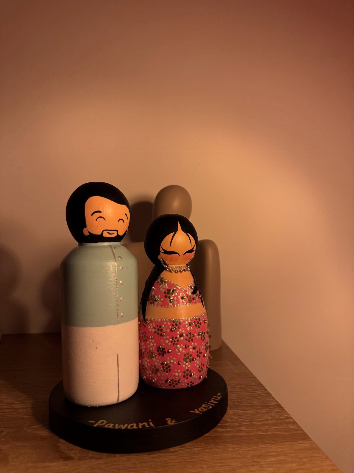 Two hand-painted wooden peg dolls of a couple on a black base.