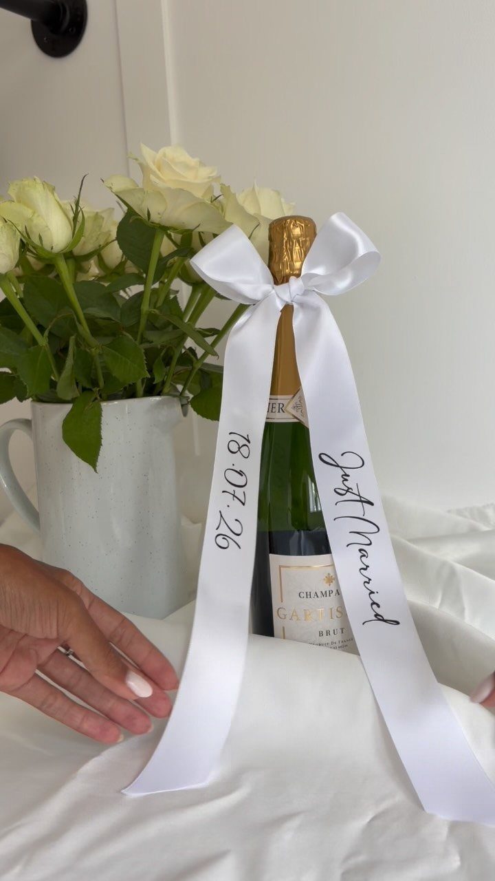 Champagne bottle with a white 'Just Married' ribbon next to white roses.
