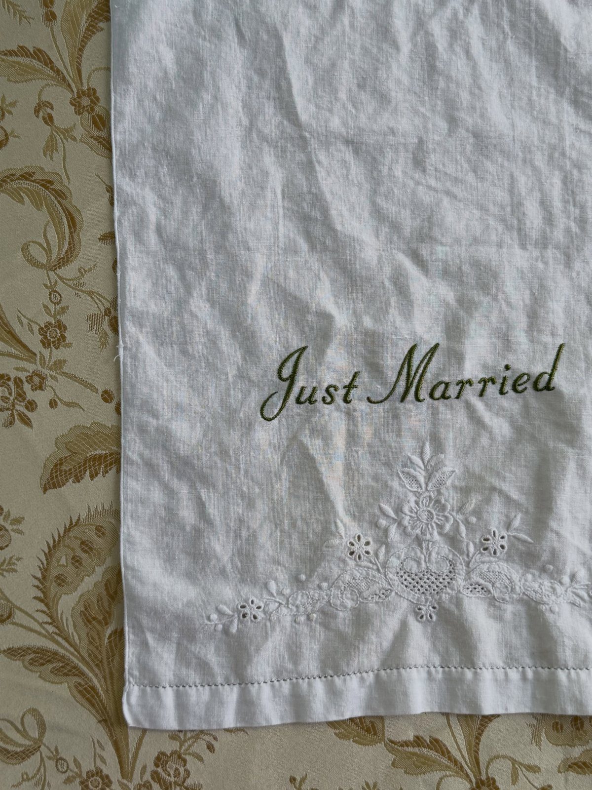 White linen tea towel with green Just Married embroidery and white floral details.