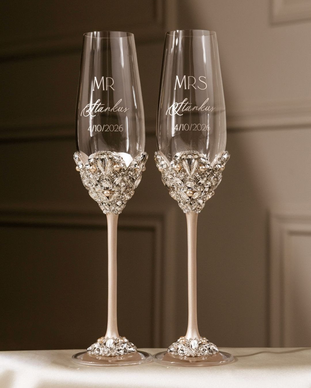 Two engraved champagne flutes with ornate crystal decorations for a married couple.