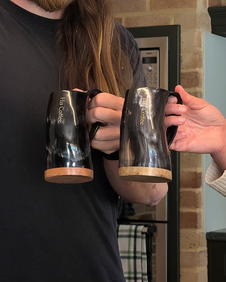 Two black engraved coffee mugs held by a couple in a kitchen setting.