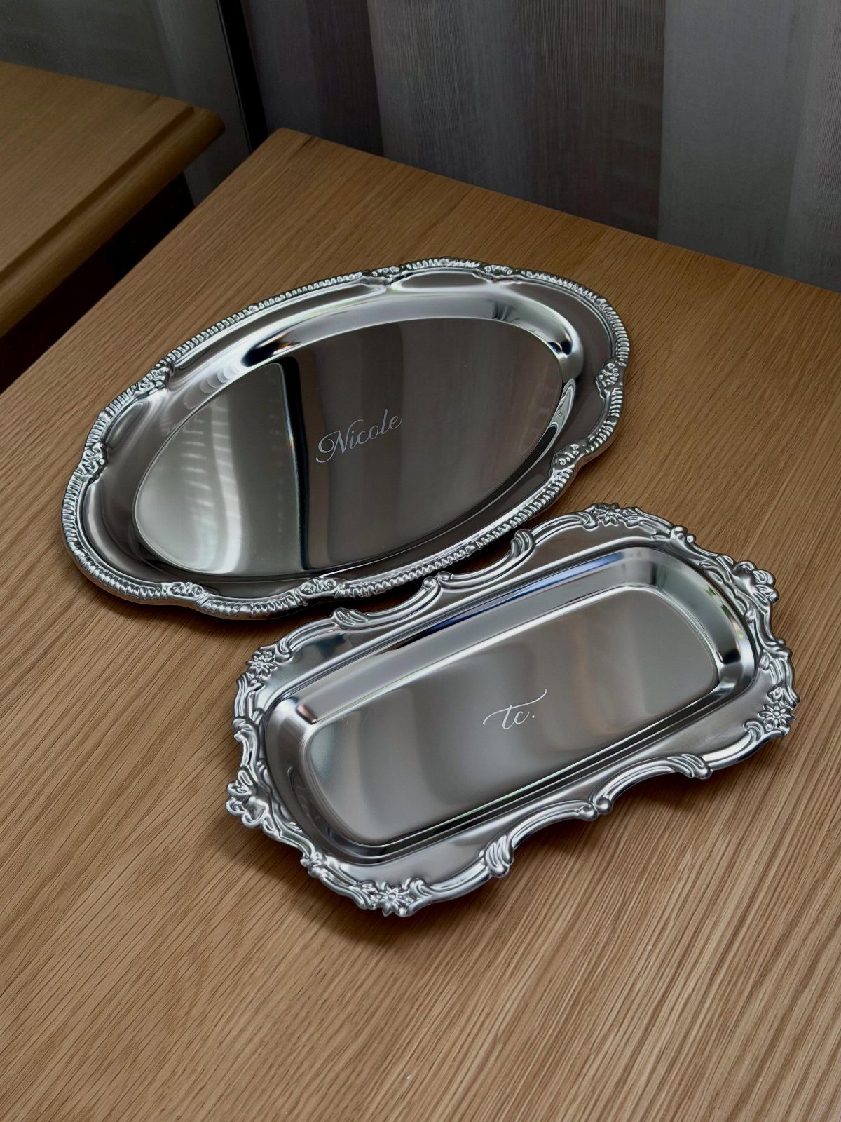Two engraved silver trinket dishes with ornate edges on a wooden table.