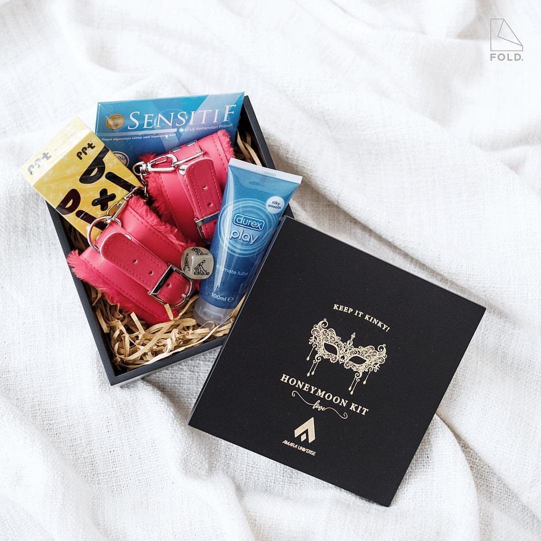 Honeymoon kit gift box with pink handcuffs, lubricant, and condoms on white fabric