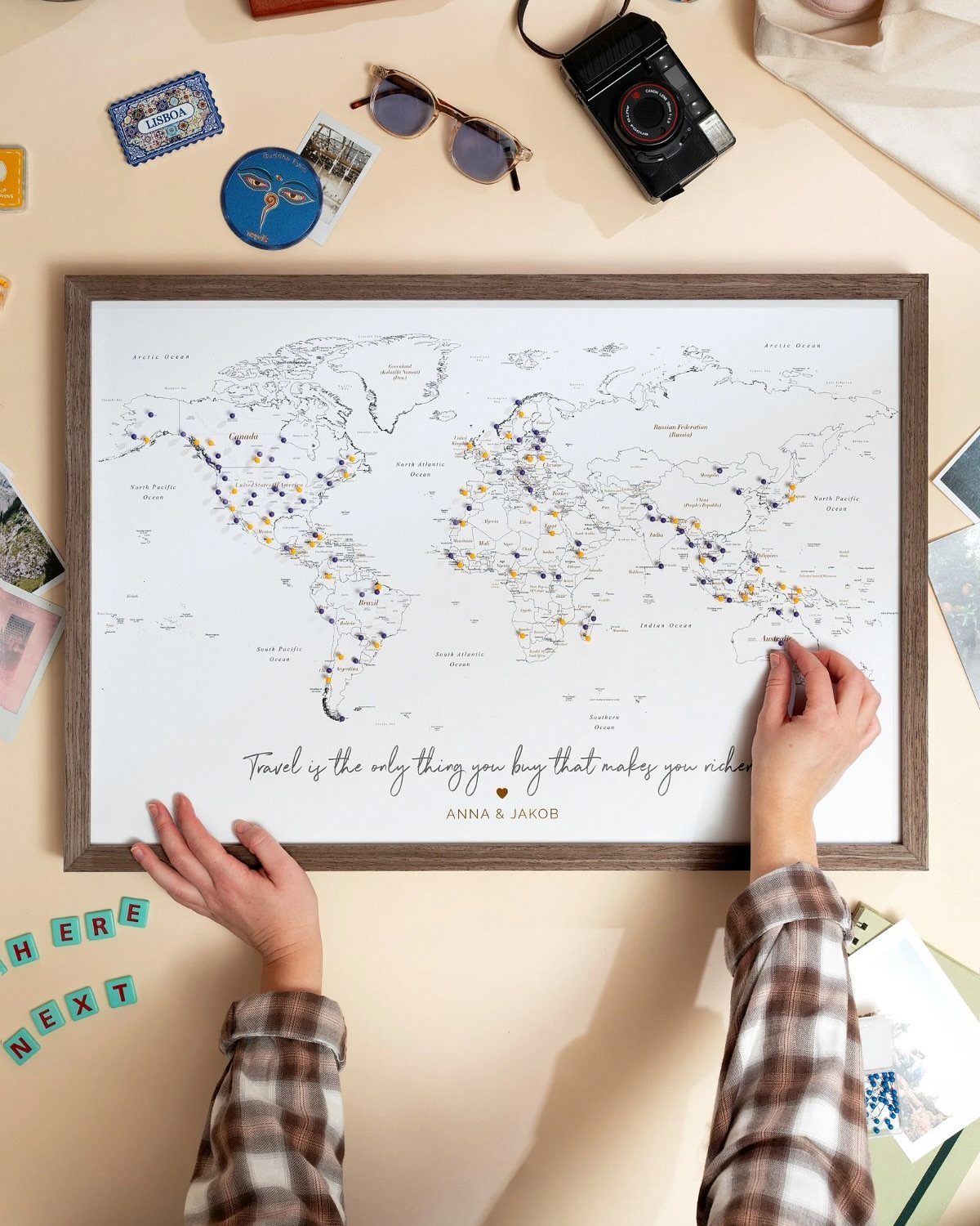 Framed world map with travel pins and names, surrounded by travel accessories.