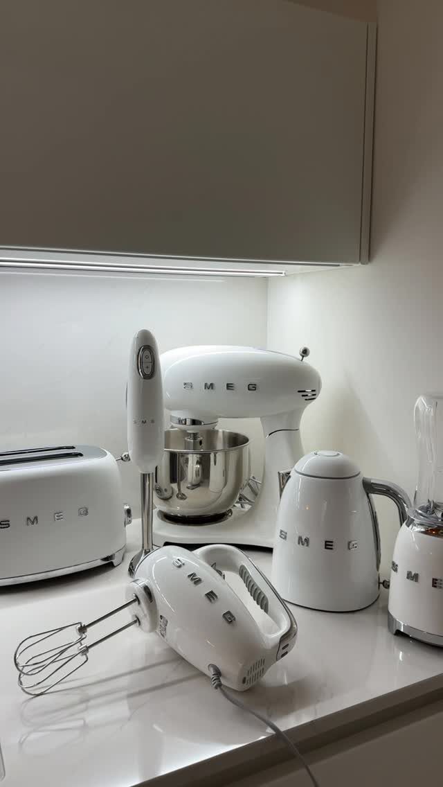 White Smeg kitchen appliances including a mixer, toaster, and kettle on a countertop.