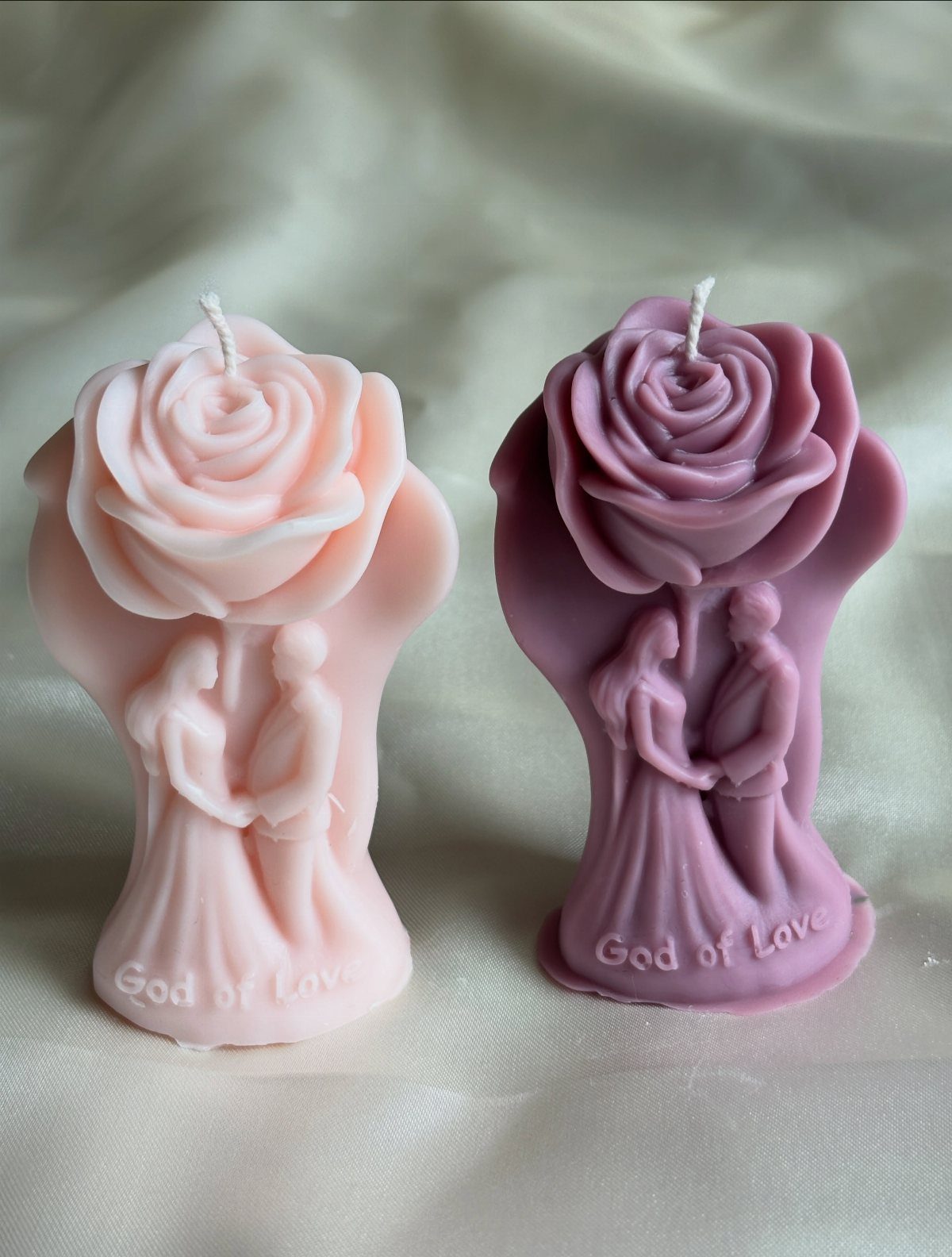 Two rose-shaped candles in pink and purple depicting a couple holding hands.