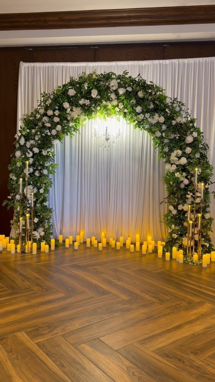 Floral wedding arch with white roses and glowing pillar candles on wooden floor
