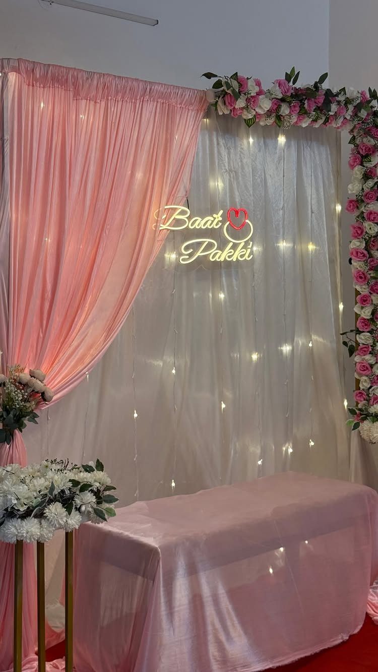 Decorative backdrop with pink and white curtains, fairy lights, and floral arrangements.