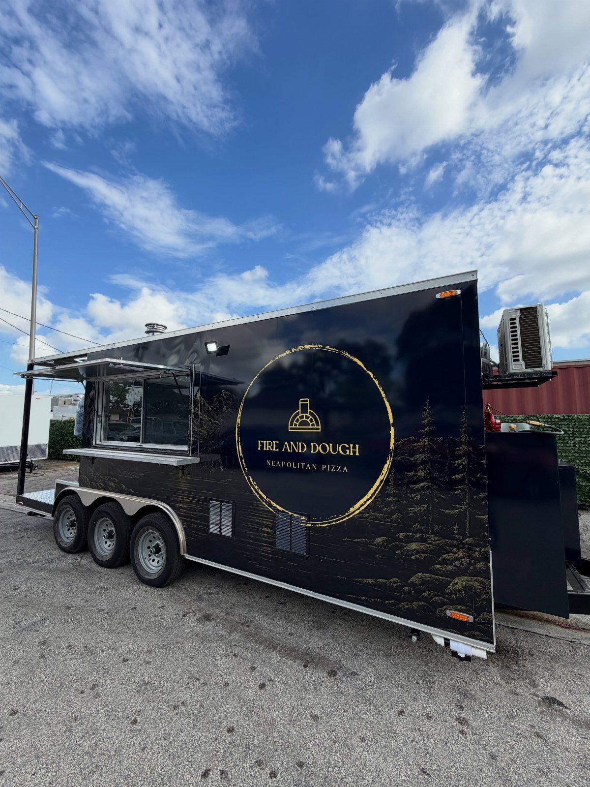 Black pizza food truck trailer with gold logo parked on an asphalt lot.