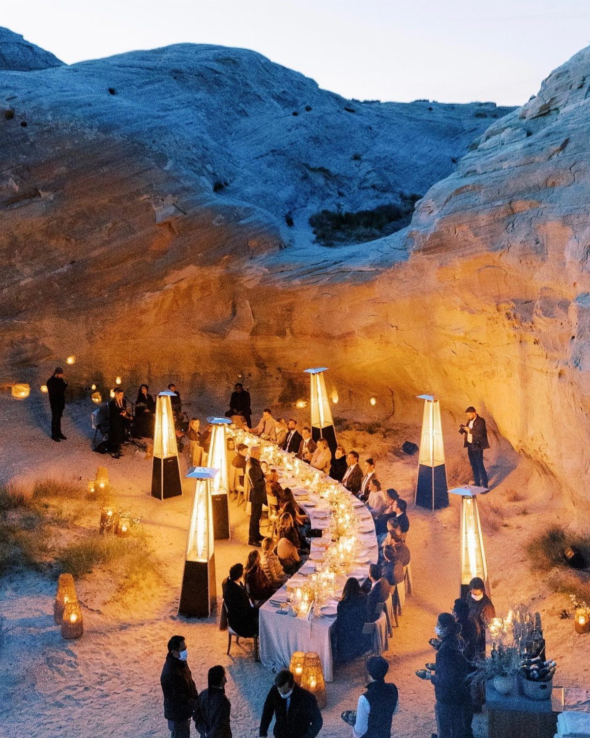 Formal dinner table set in a desert canyon with guests and warm lighting.