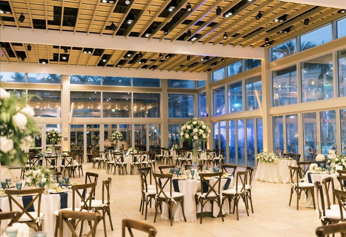 Elegant wedding reception setup with white floral centerpieces and ocean views through glass walls.