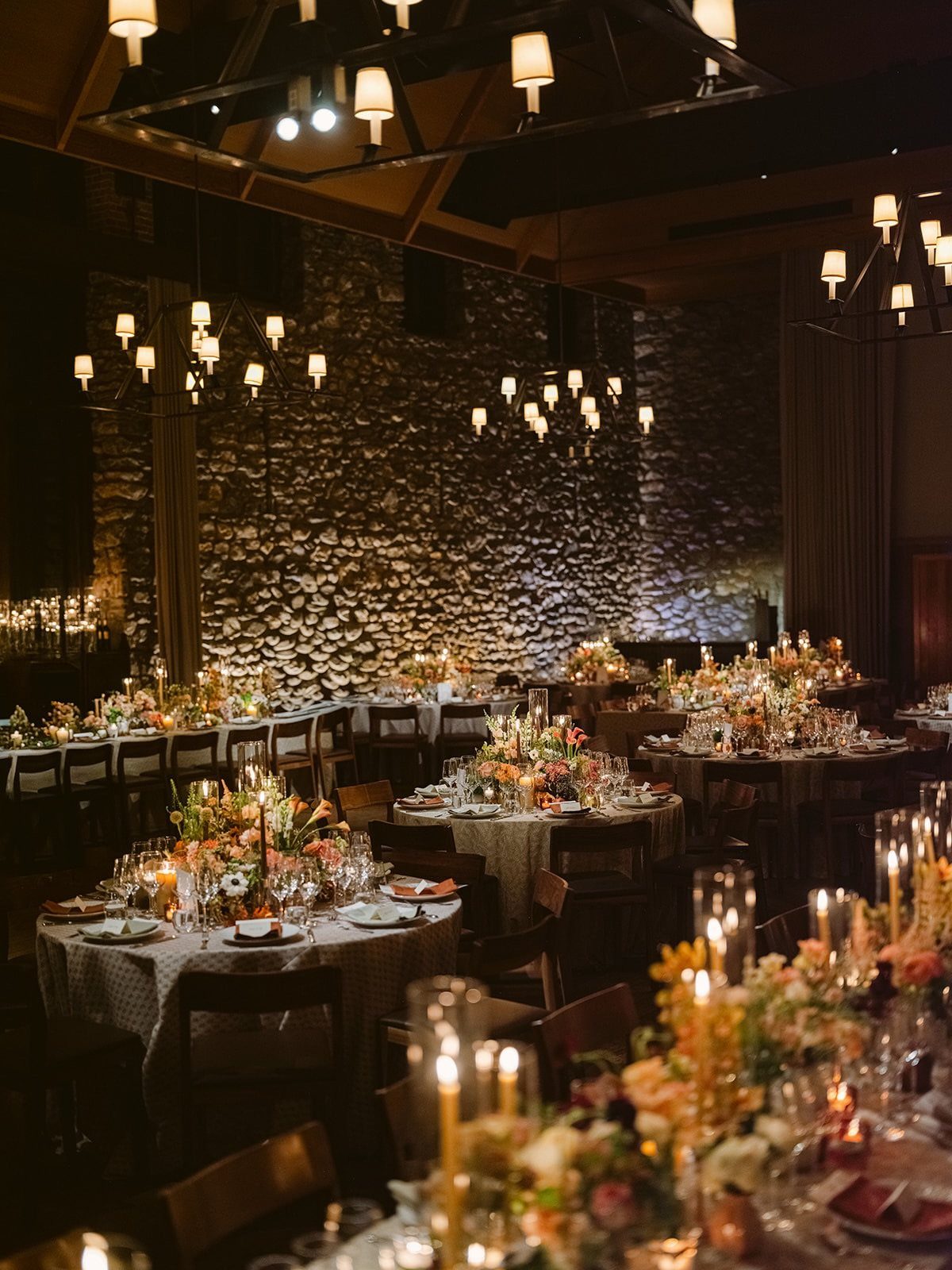 Elegant dining room with stone walls, candlelit tables, and floral wedding centerpieces.