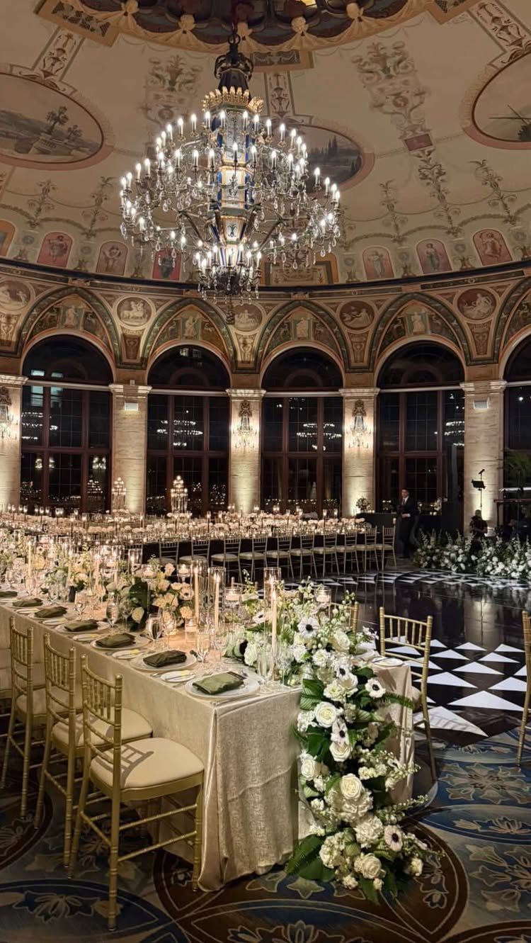 Opulent ballroom with a crystal chandelier and long table decorated with white flowers.