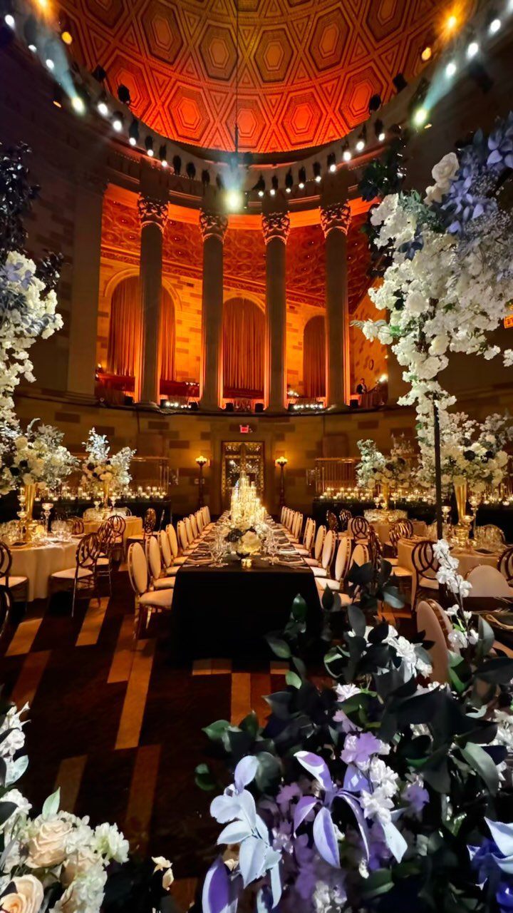 Grand banquet hall with orange ceiling, tall columns, and long floral wedding table.