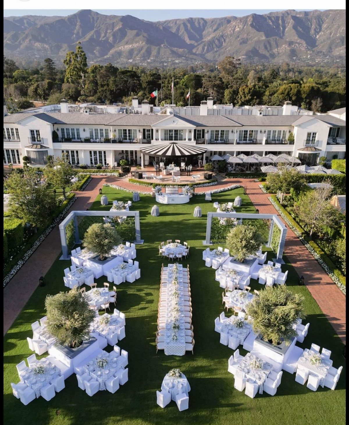 Outdoor wedding reception with white tables and chairs on a lawn before a mansion.
