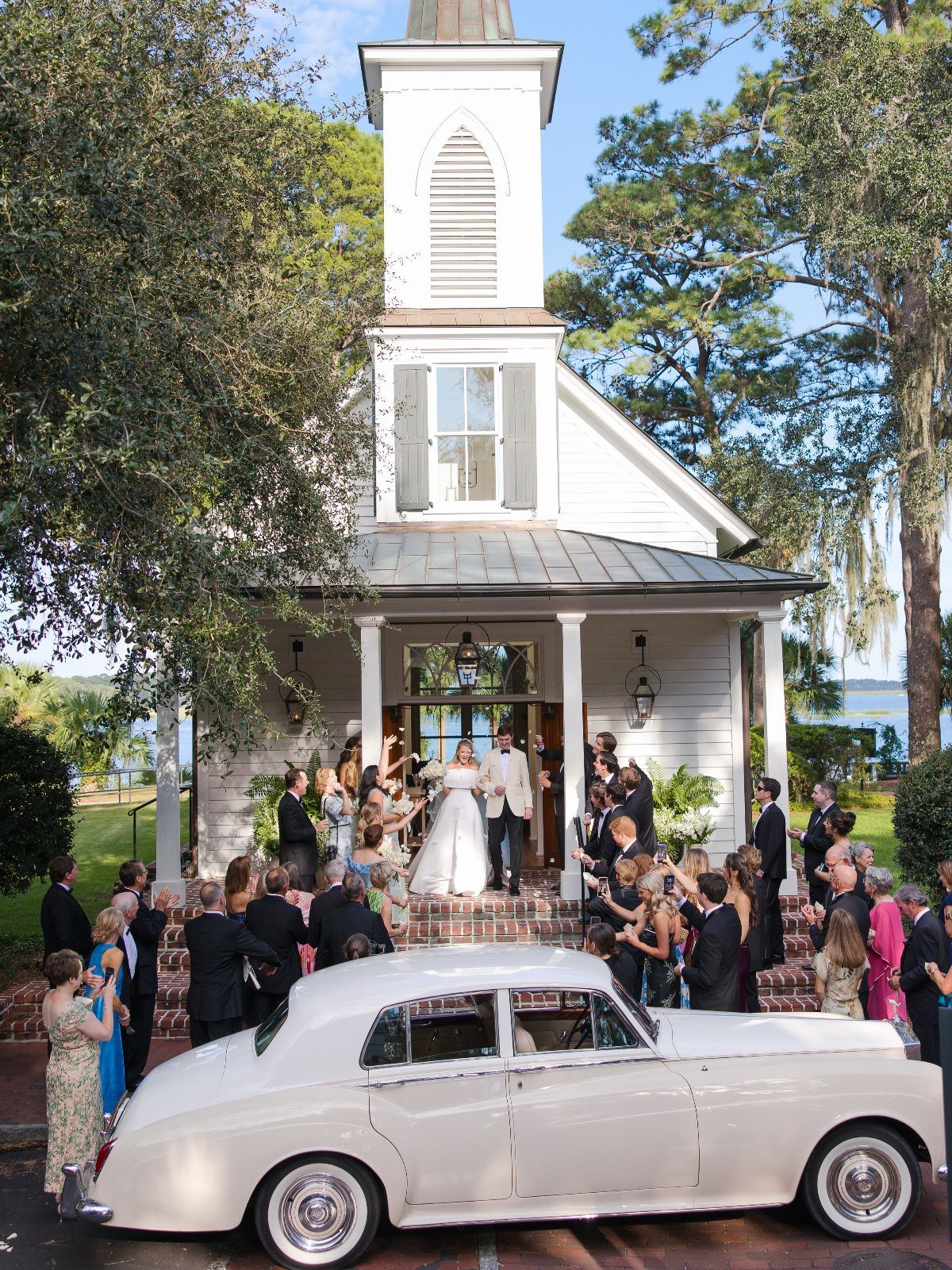 Bride and groom at a white chapel entrance with a vintage white car.