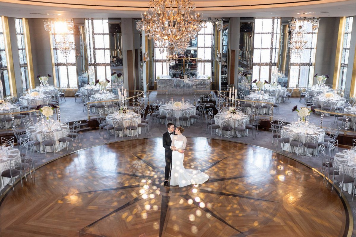 Bride and groom embracing on a wooden dance floor in a luxury ballroom.