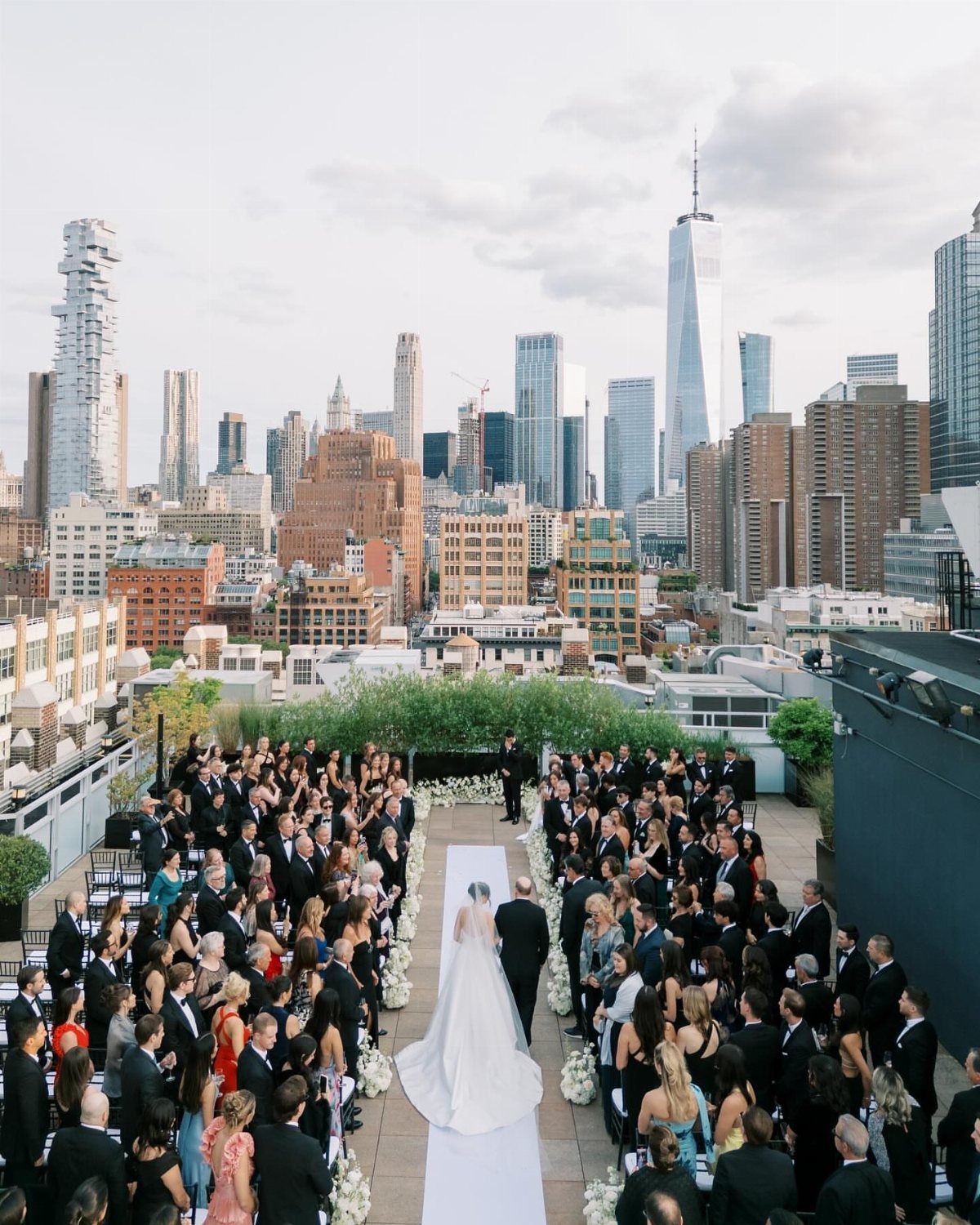Bride walking down a white aisle at a rooftop wedding with NYC skyline views.