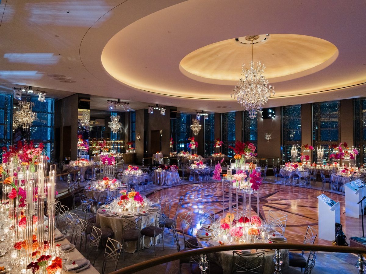 Luxurious wedding ballroom with pink floral centerpieces and crystal chandeliers overlooking city skyline