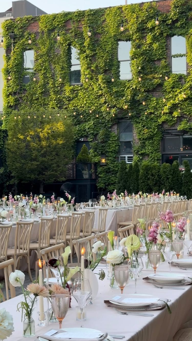 Long formal dining table with floral arrangements in an ivy-covered urban courtyard